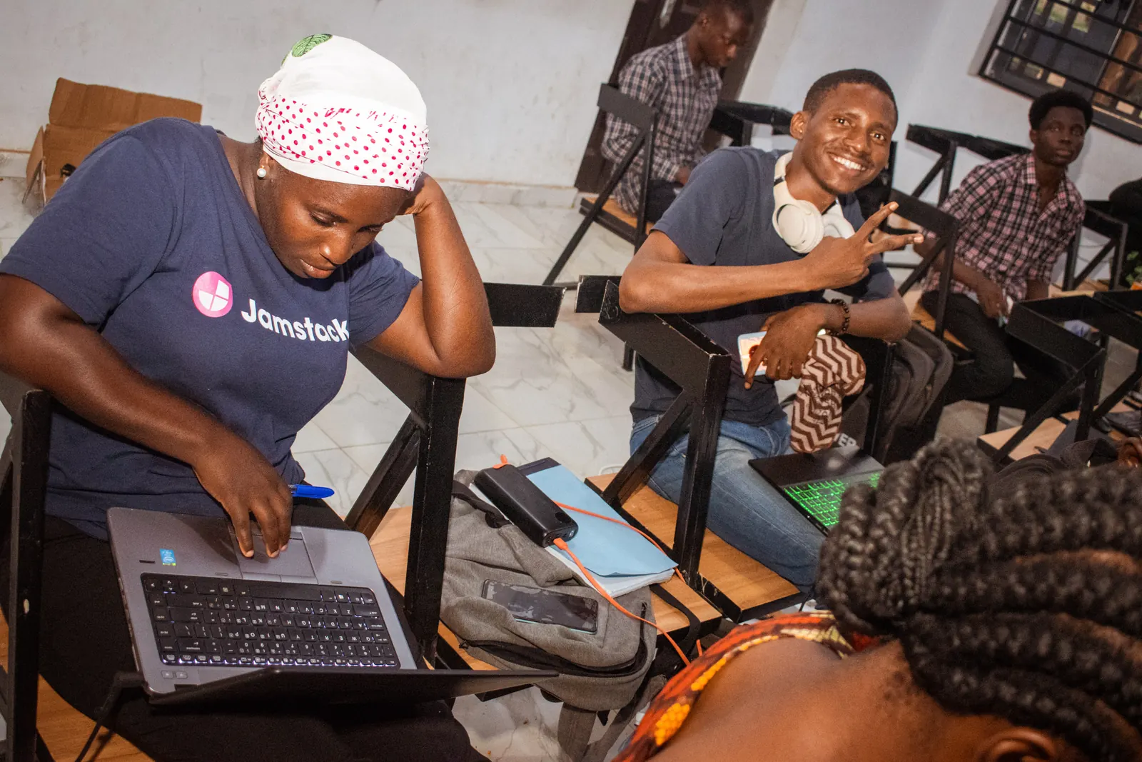 Students working on laptops together in a lecture hall, one of them smiling at the camera.